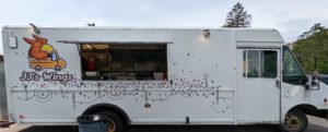 The JJ's Wings food truck - a long, white food truck with the JJ's logo (a truck with chicken wings on its sides), a thin stencil running the length of the truck, and dozens of little stickers