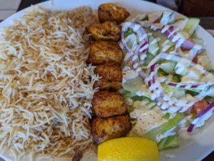 Platter with a large portion of seasoned rice on the right, garden salad with a creamy dressing drizzled on top on the left, divided down the middle with chunks of grilled chicken breast tikka - Salang Kabob House