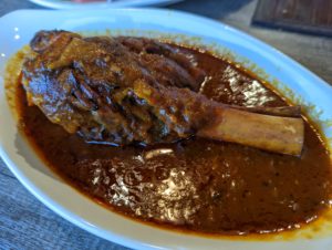 Lamb shank in its braising sauce on a white platter - Salang Kabob House