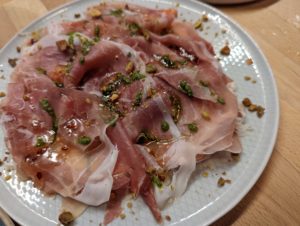 Fruits 'n' 'Sciut - layers of thinly-cut prosciutto on a white plate, topped with bits of pistachio and dribbles of honey and pesto - Fraser Restaurant